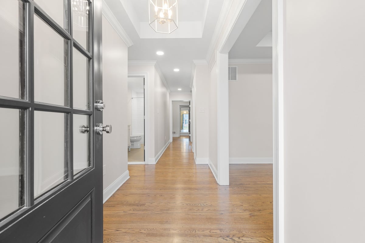 Black front door opening to remodeled home in Delaware with modern light pendant hanging from coffered ceiling