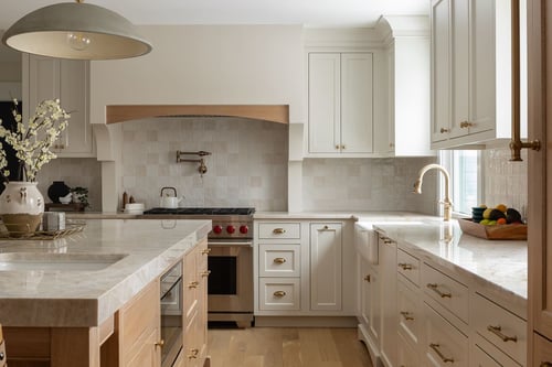 Bright kitchen remodel with marble island, white cabinetry, brass hardware, wood accents, and pendant lighting.