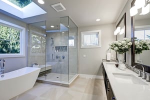 Newly remodeled bathroom with porcelain tub, walk-in shower with glass enclosure, tile flooring, and twin vanity mirrors