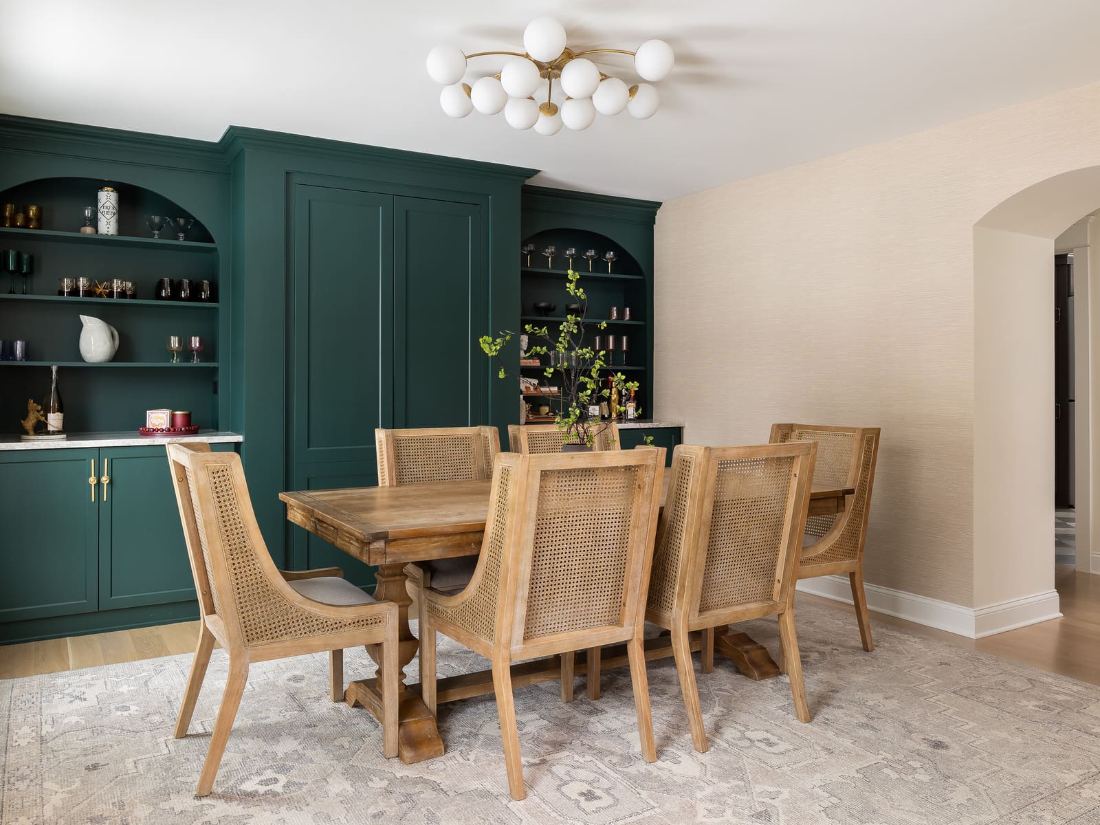 Bright dining room remodel with teal built-ins, wood table, cane chairs, arched doorway, and patterned rug.