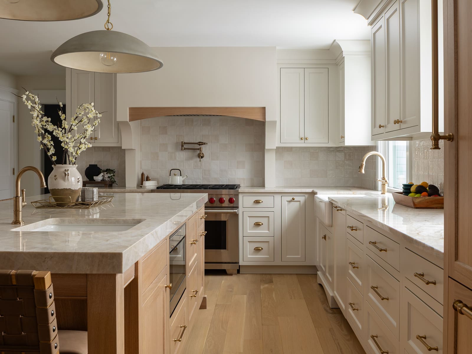 Bright kitchen remodel with marble island, white cabinetry, brass hardware, wood accents, and pendant lighting.
