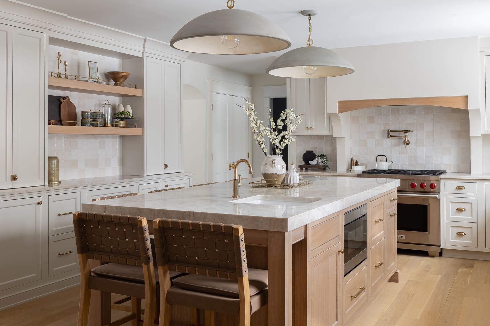 Bright kitchen with large marble island, white cabinetry, open wood shelves, pendant lights, and bar seating.
