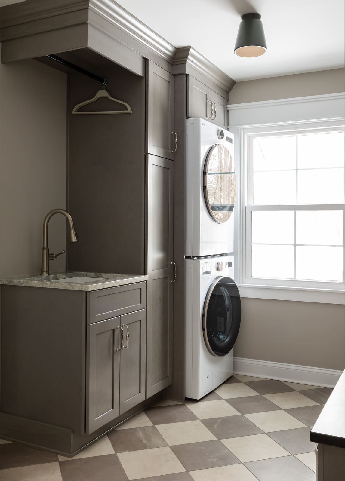 Bright laundry room with stacked washer and dryer, gray cabinetry, utility sink, and checkerboard tile floor.
