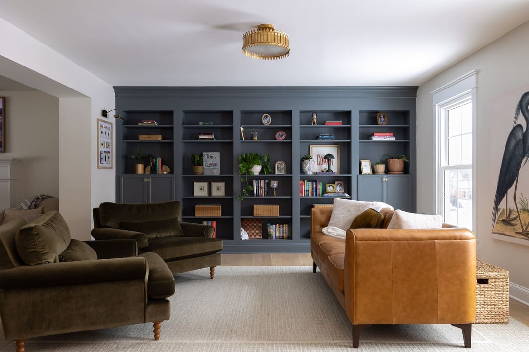 Bright living room remodel with blue-gray built-in bookshelves, leather sofa, armchairs, and large area rug.