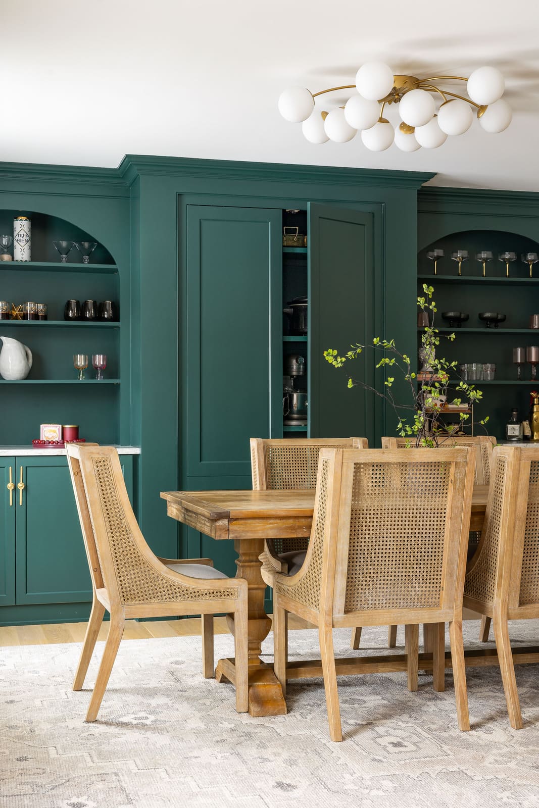 Dining room remodel with teal built-in storage, open shelving, wood table, cane chairs, and globe light fixture.