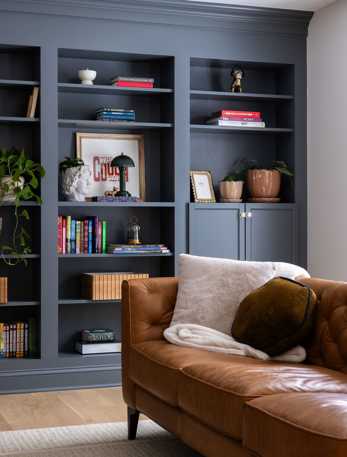 Living room built-ins with blue-gray bookshelves, cabinet storage, books, plants, and leather sofa.