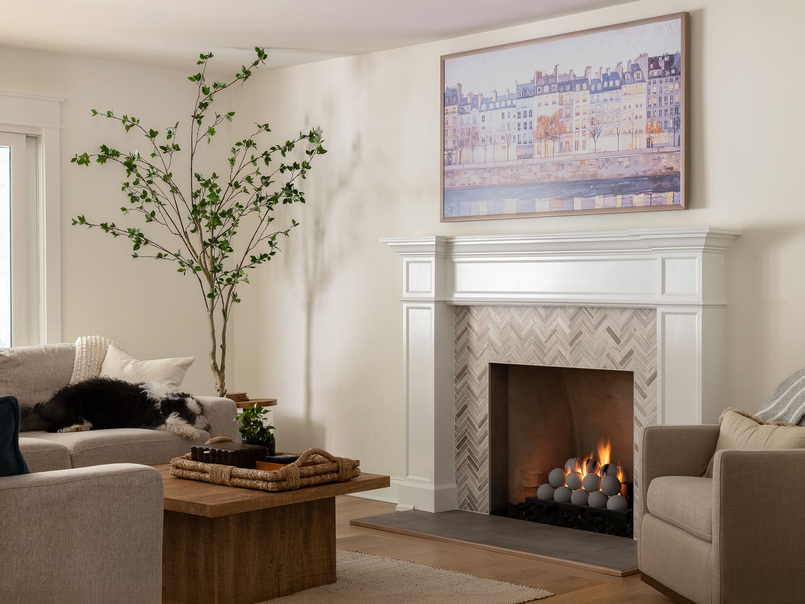 Living room fireplace remodel with white mantel, herringbone tile, wood coffee table, and neutral seating.