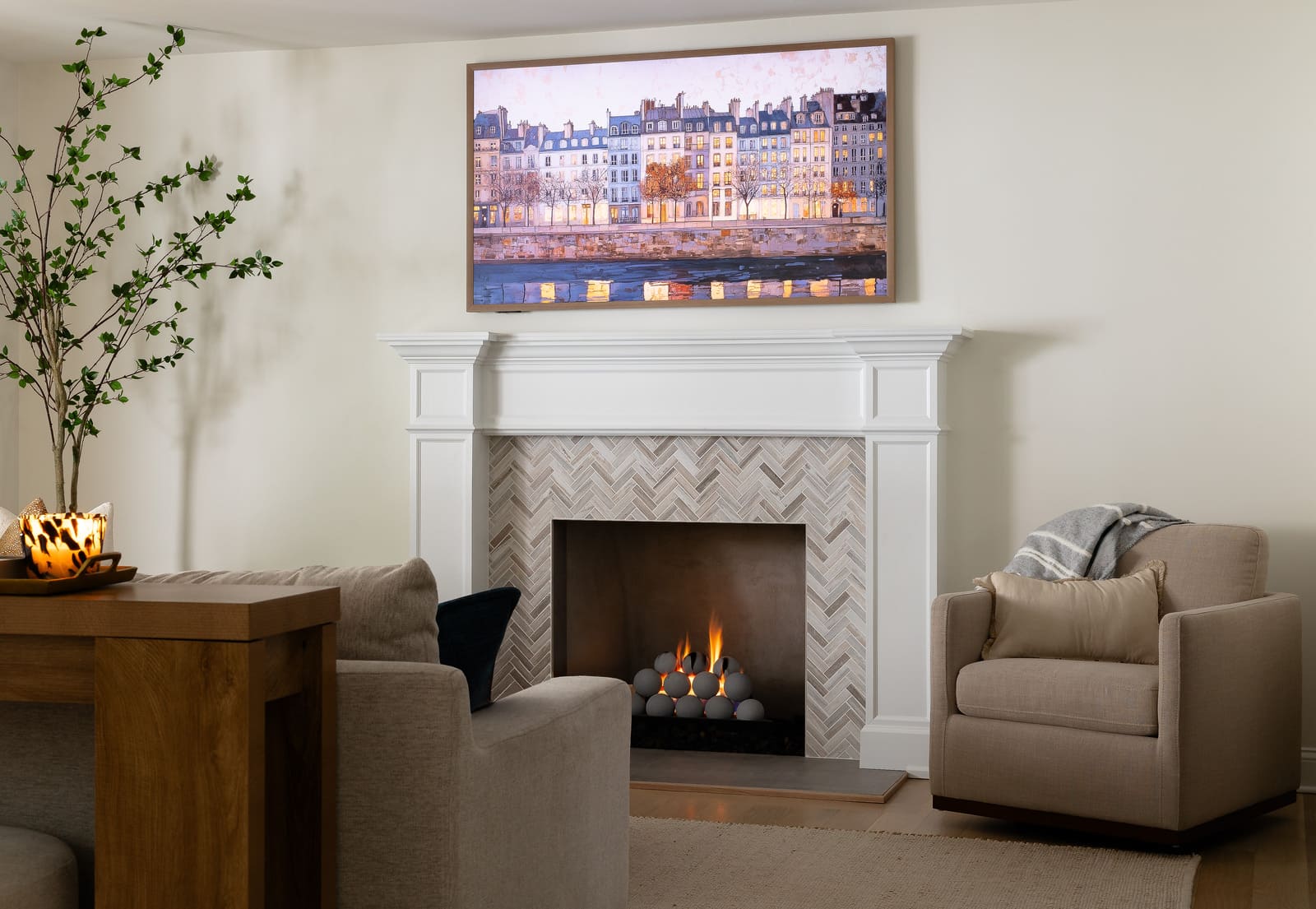 Living room remodel with white fireplace mantel, herringbone tile, framed TV art, and cozy seating.