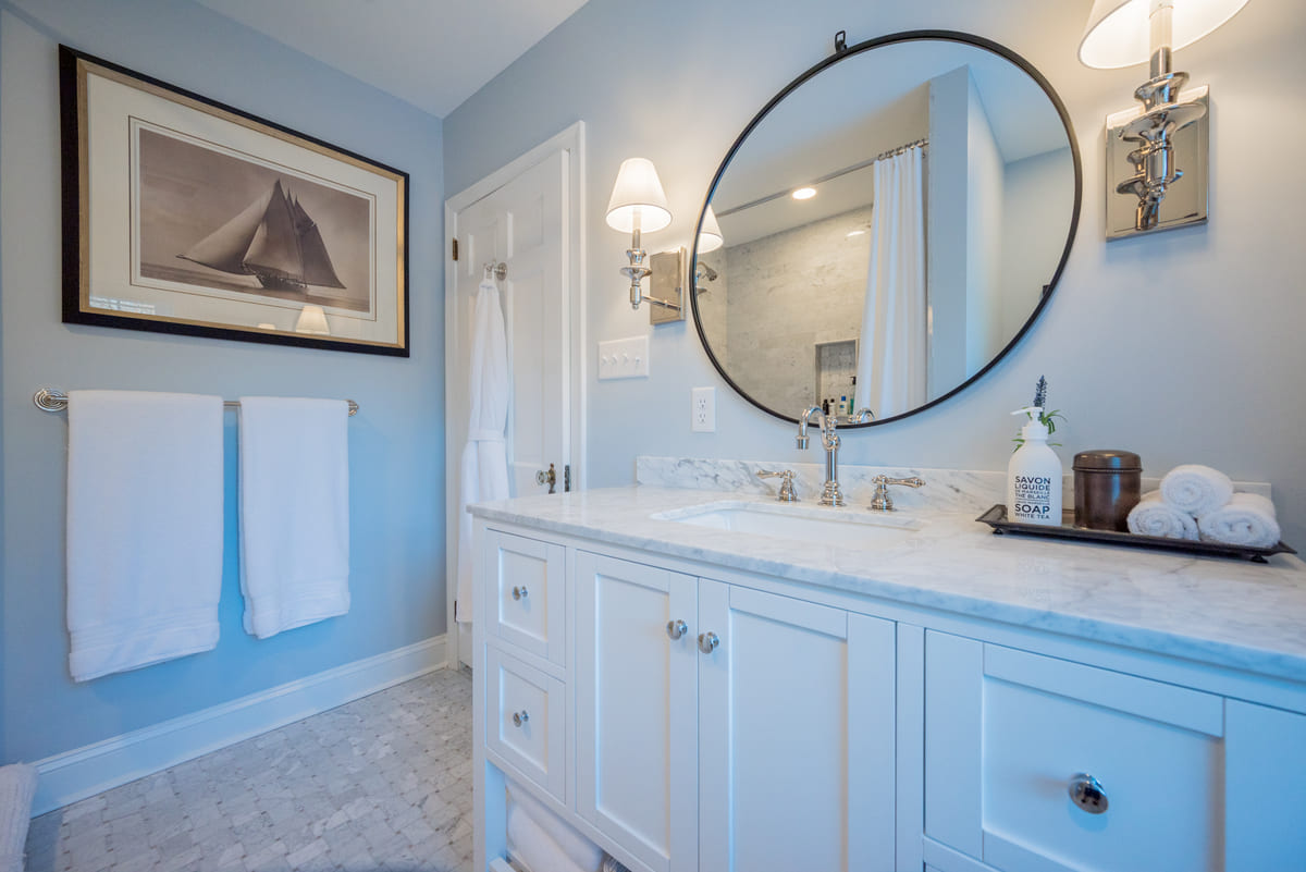 Circular mirror between two light sconces in Delaware bathroom remodel with white vanity