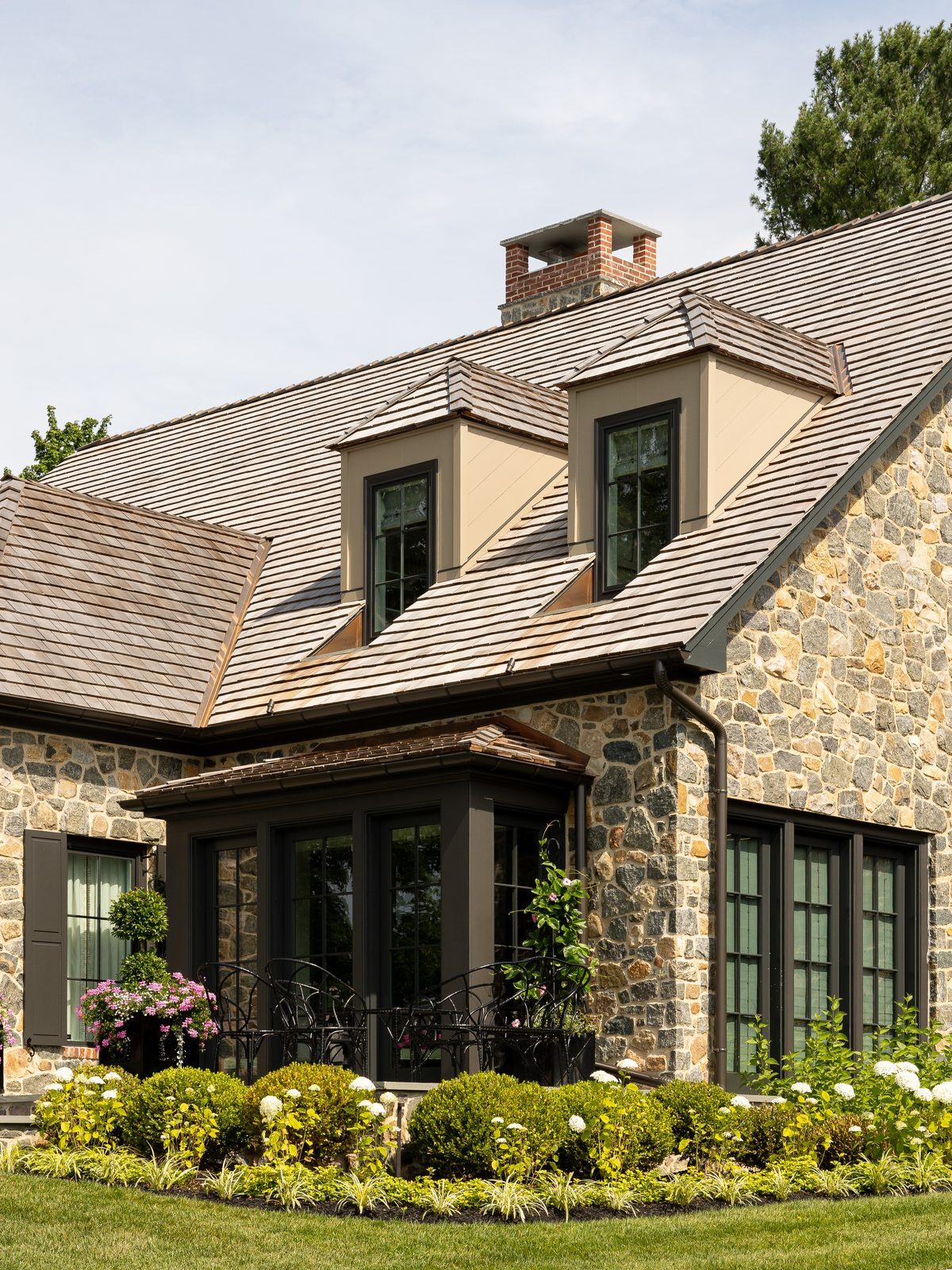 Close-up daytime view of dormer windows and chimney with bay window and hydrangeas