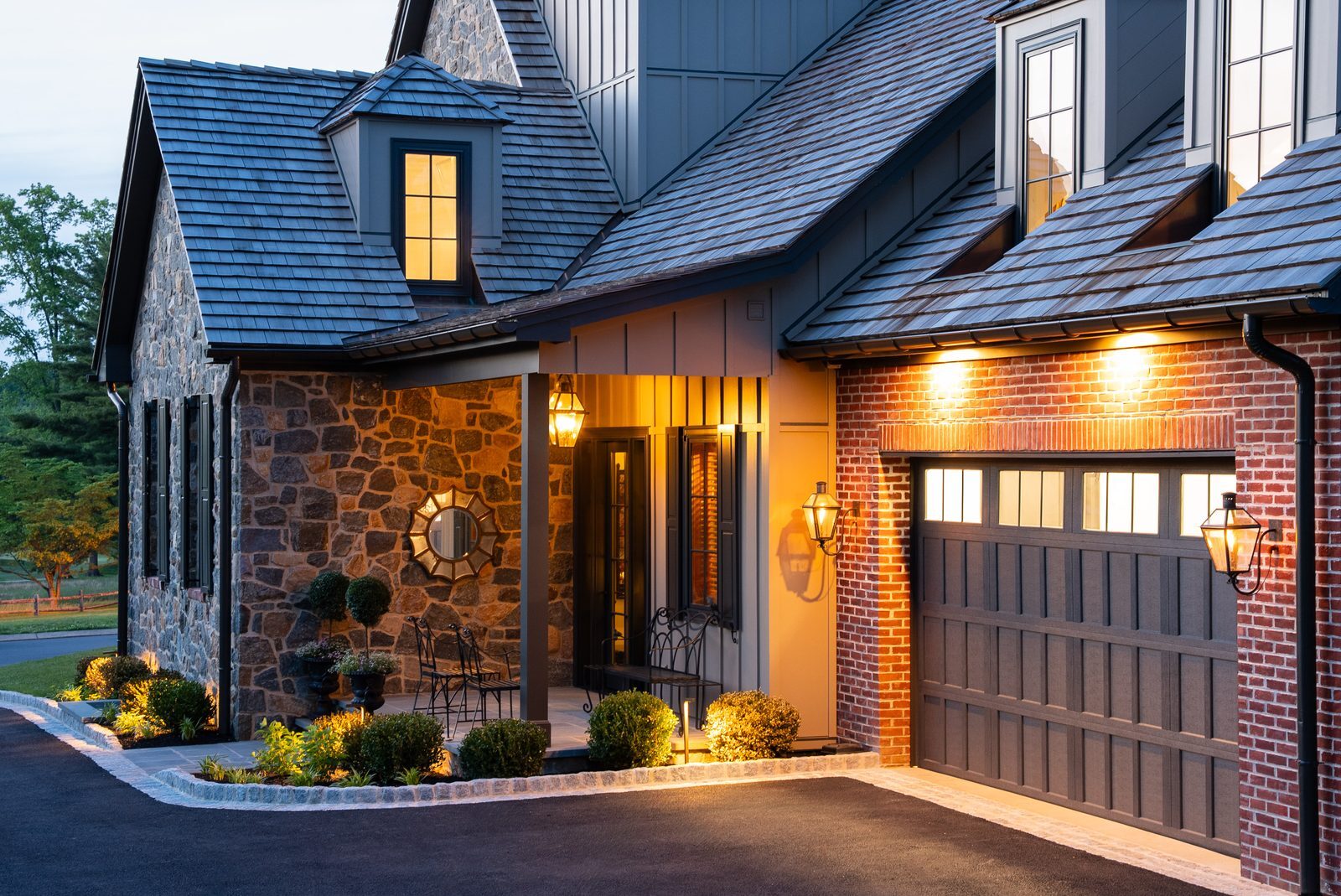 Close-up dusk view of covered porch with sunburst mirror and brick garage