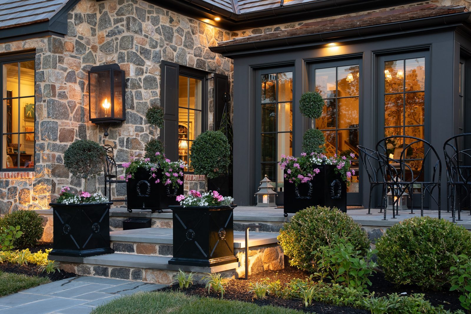 Close-up dusk view of stone entry patio with lit lantern and manicured topiaries
