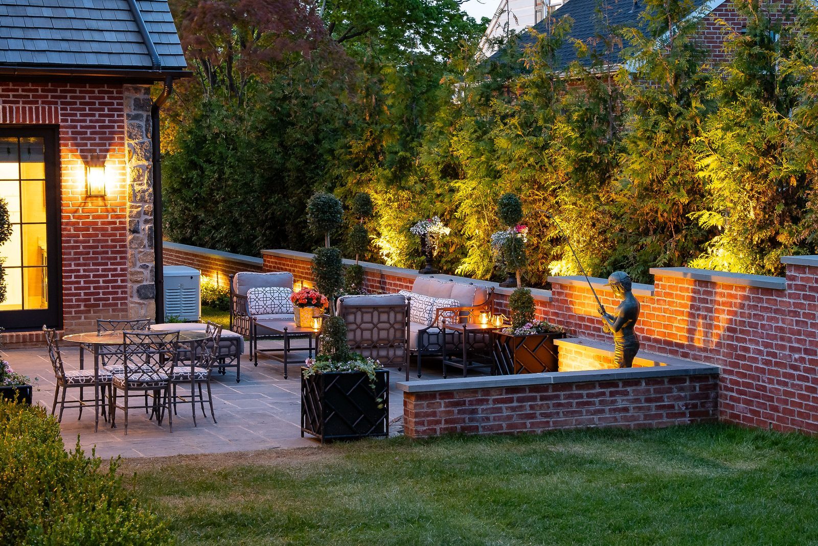 Dusk view of brick-walled patio with cushioned seating and fountain statue