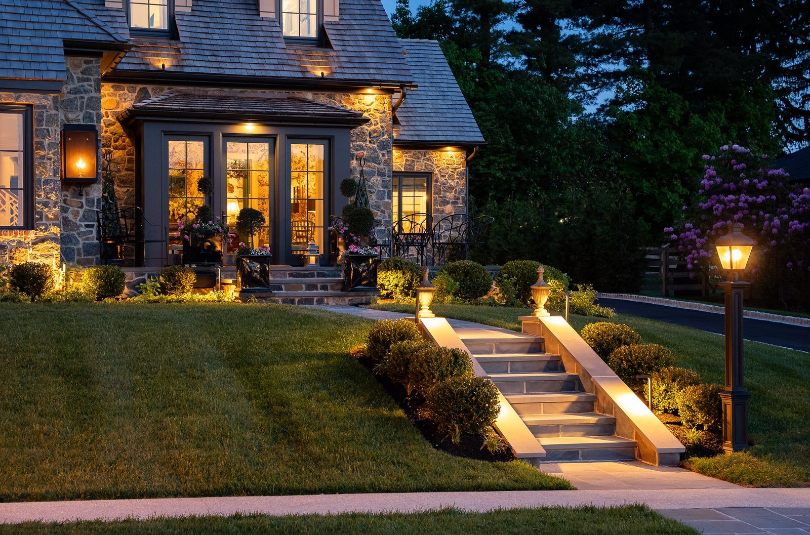 Dusk view of lantern-lit walkway leading to glass sunroom entrance