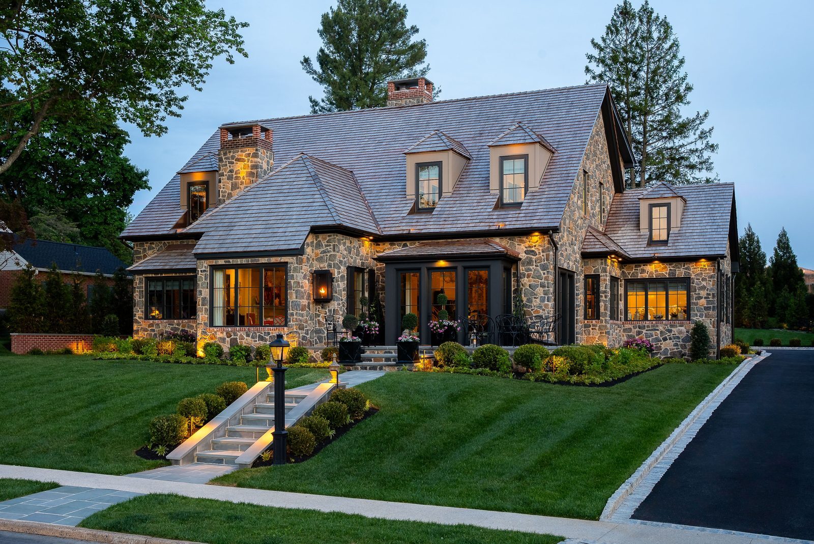 Front-facing dusk view of stone home with brightly lit entry and silhouetted chimney