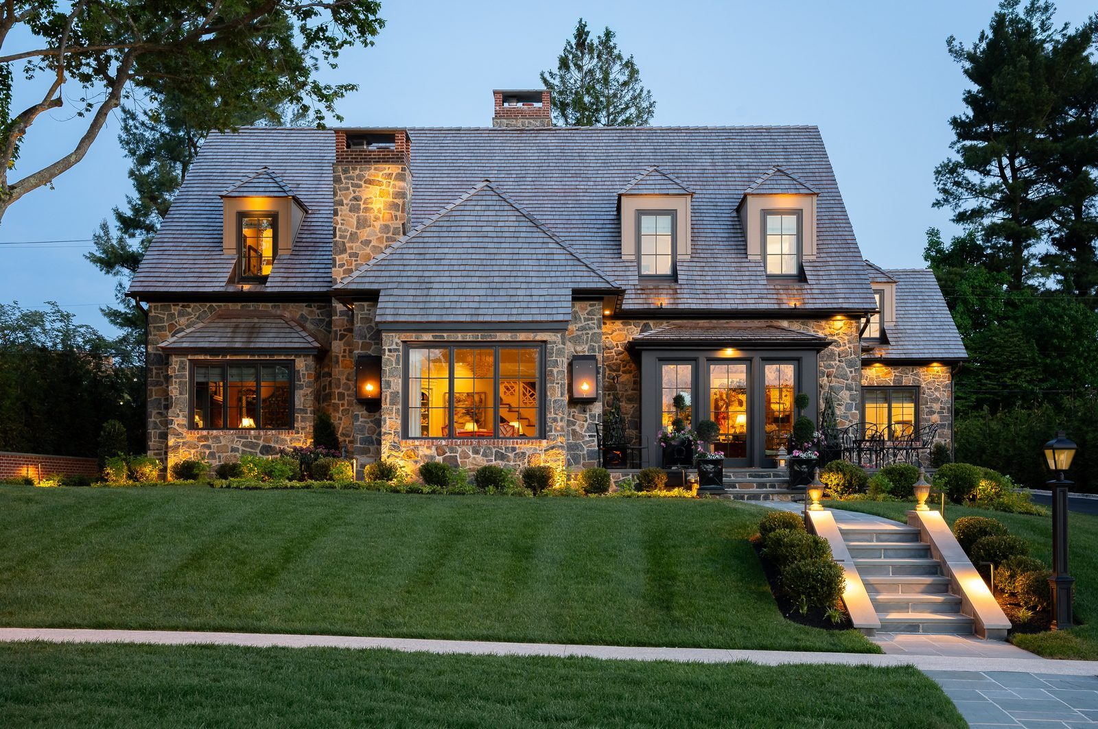Front-facing dusk view of stone home with glowing windows and lit walkway