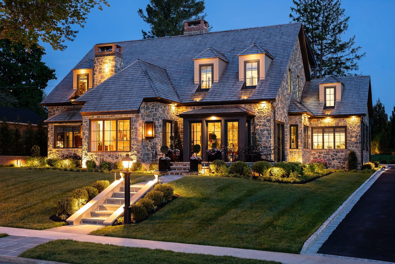 Front-facing twilight view of stone home with warmly lit windows and walkway