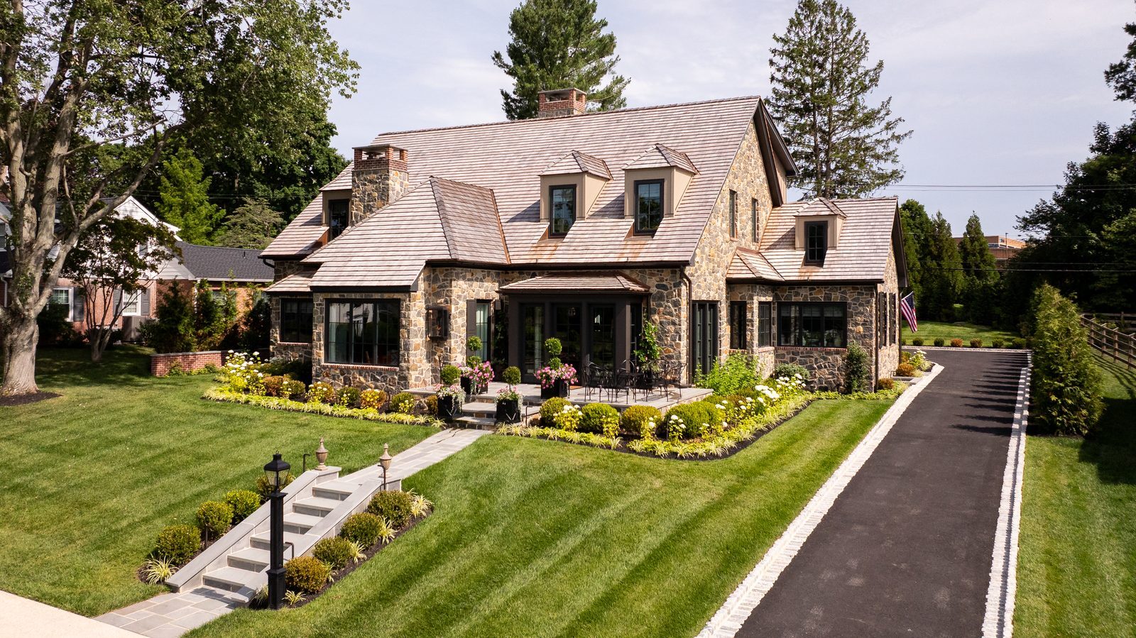 Wide aerial daytime view of stone home facade, expansive lawn, and curved driveway