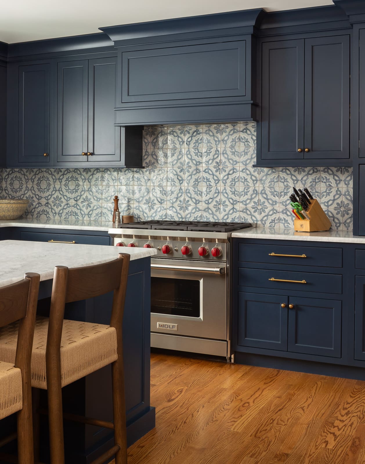 Blue kitchen cabinets with patterned tile backsplash, marble island, brass hardware, and stainless Wolf range.