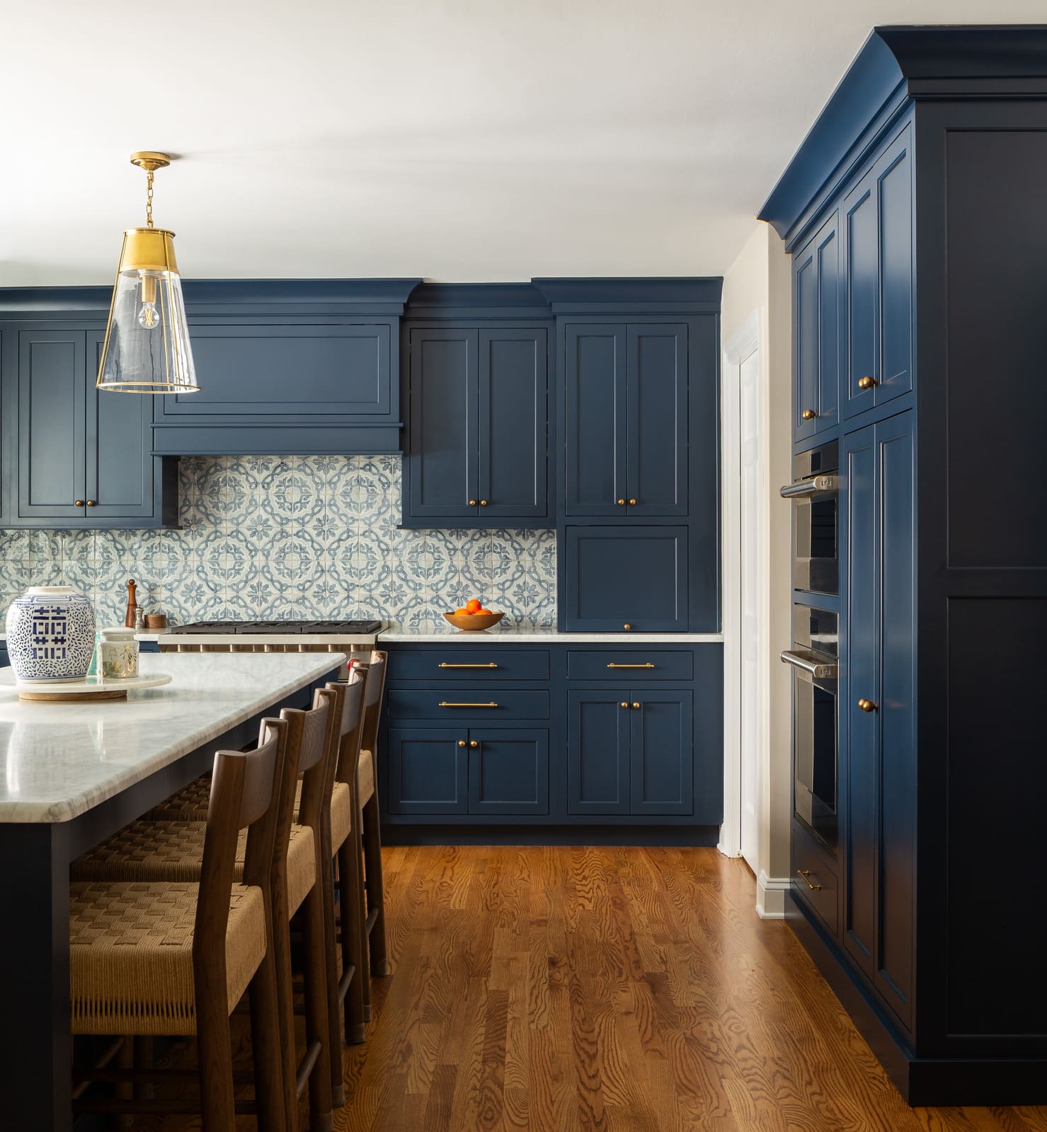 Bright remodeled kitchen with navy cabinets, patterned tile backsplash, marble island, and brass pendant light.