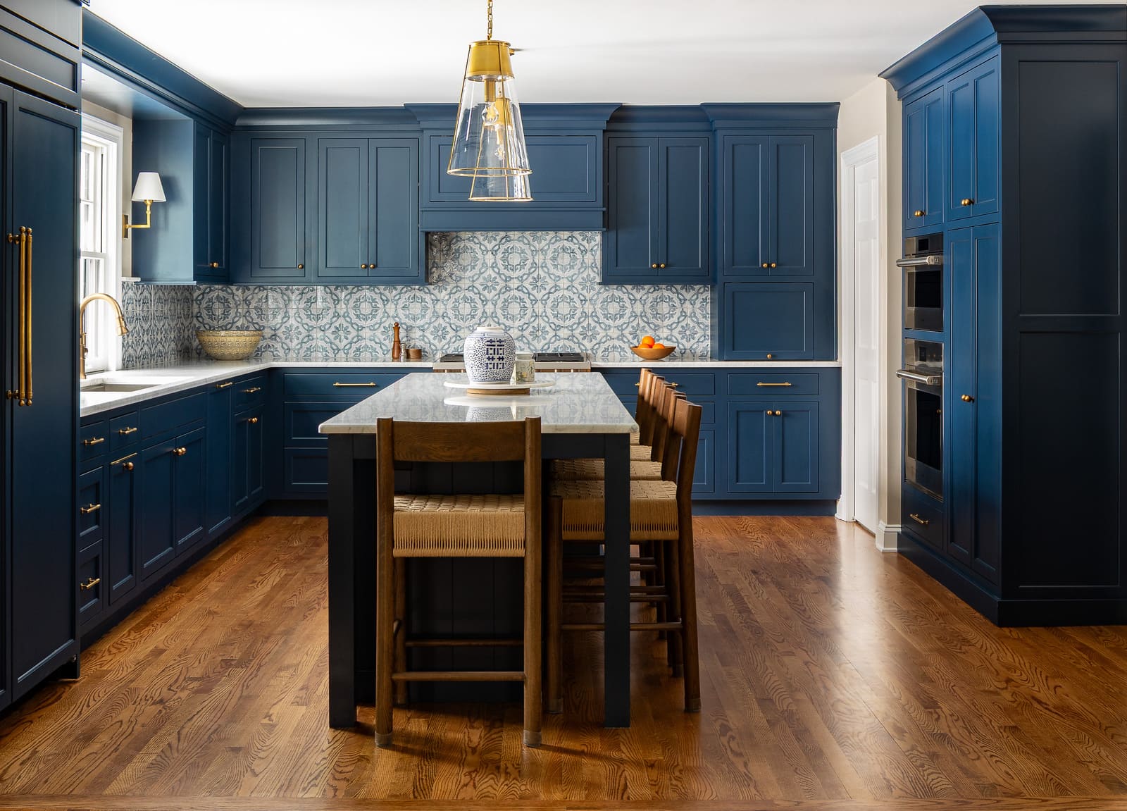 Full remodeled kitchen with navy cabinets, marble island, brass pendants, patterned tile, and wood floors.