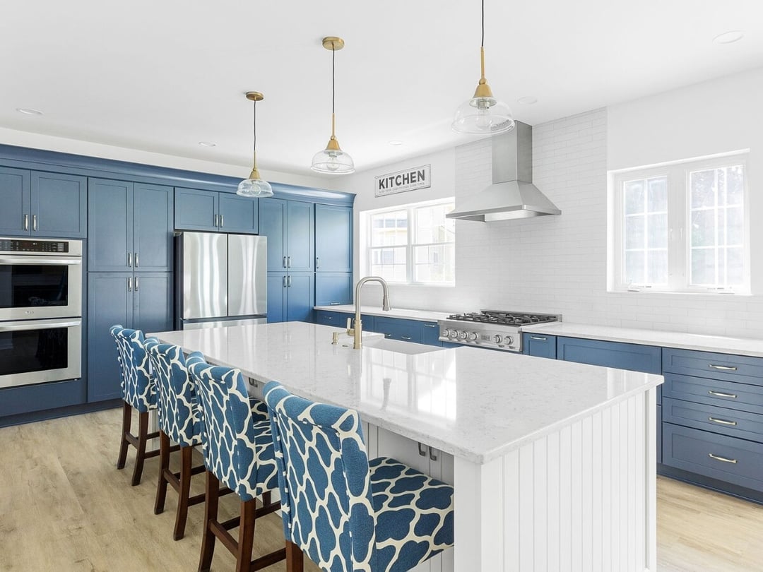 Modern kitchen with blue cabinets, white island, pendant lights, and patterned barstools by Bromwell Construction