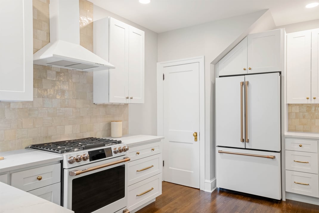 Modern white kitchen with gold hardware, tile backsplash, and hardwood floors located in the Delaware area