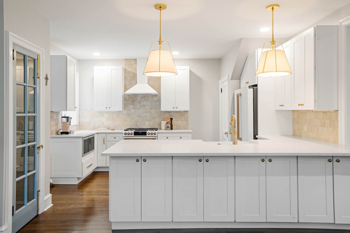 Two hanging light fixtures above L-shaped kitchen island with sink in Delaware home remodel