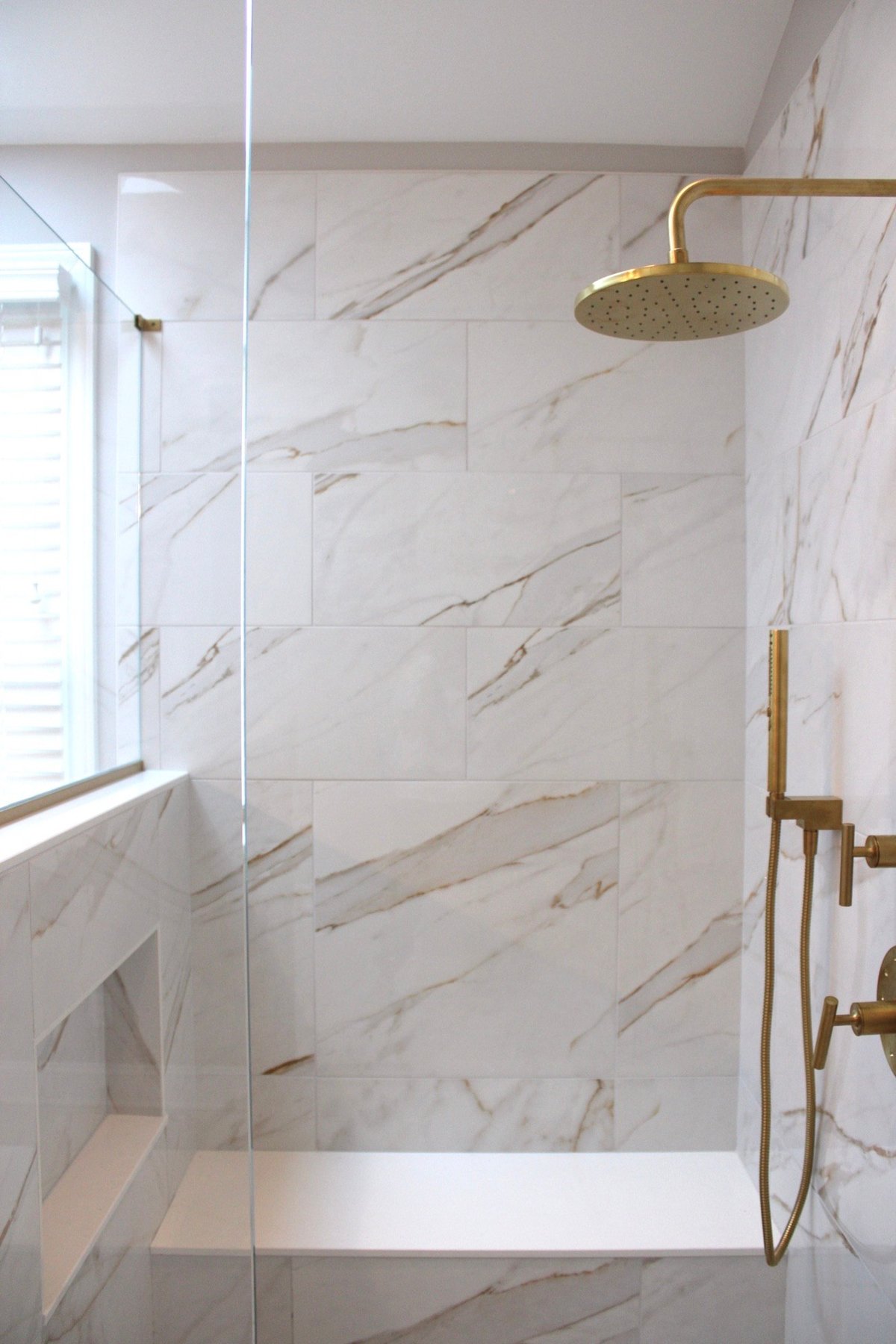 Walk-in shower with built-in bench and shelf with brass faucet fixtures in bathroom remodel by Bromwell Construction