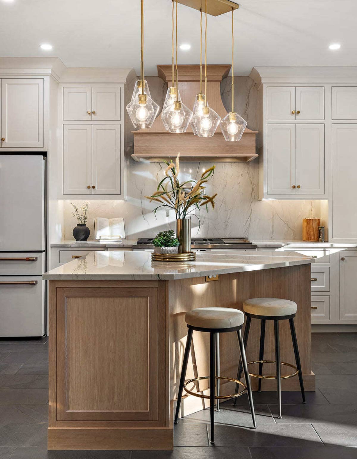 Warm kitchen with light wood island and beautiful brass pendant lights by Bromwell Construction
