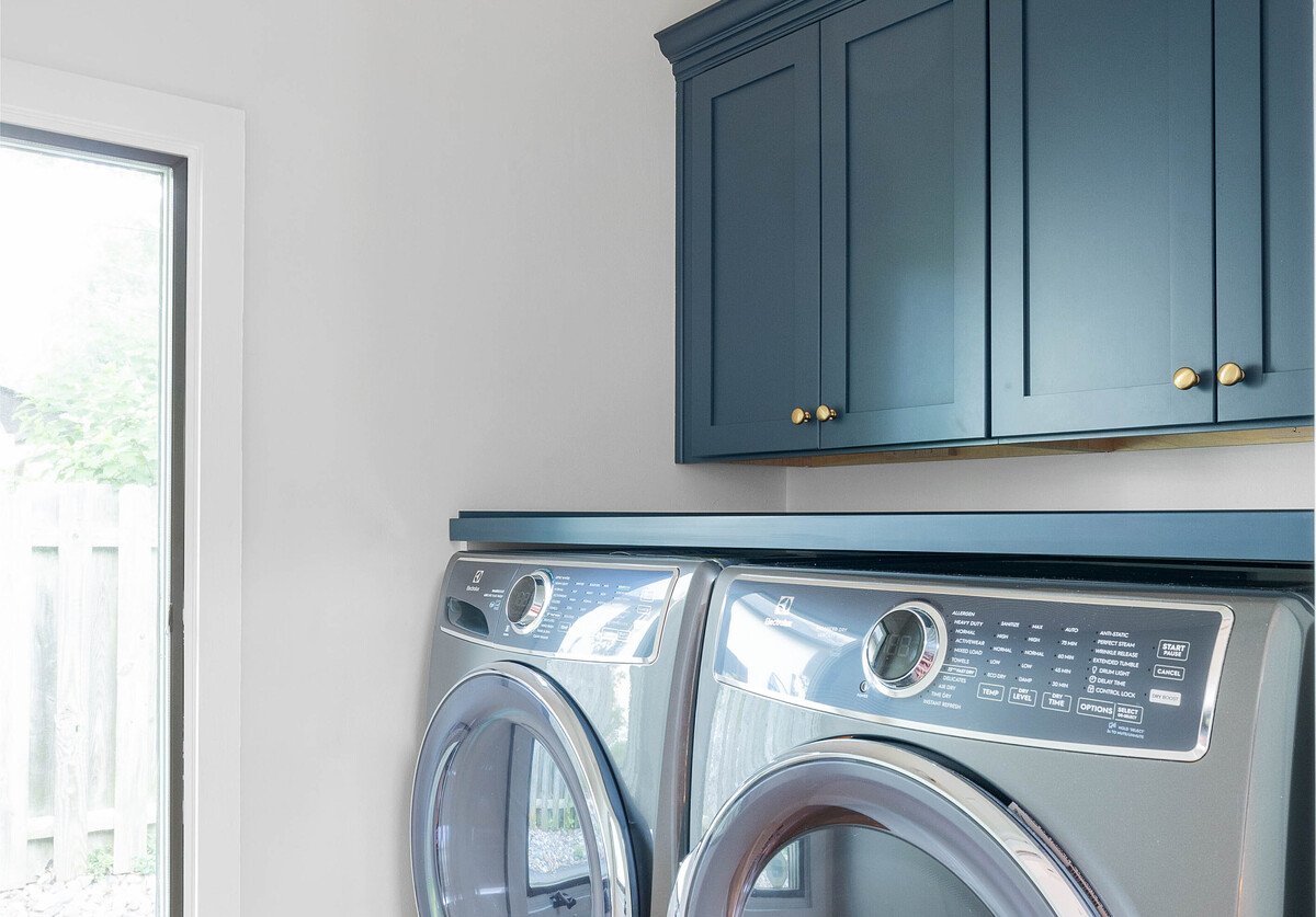 Washing and drying machine in laundry room with blue cabinets above in Delaware home remodel