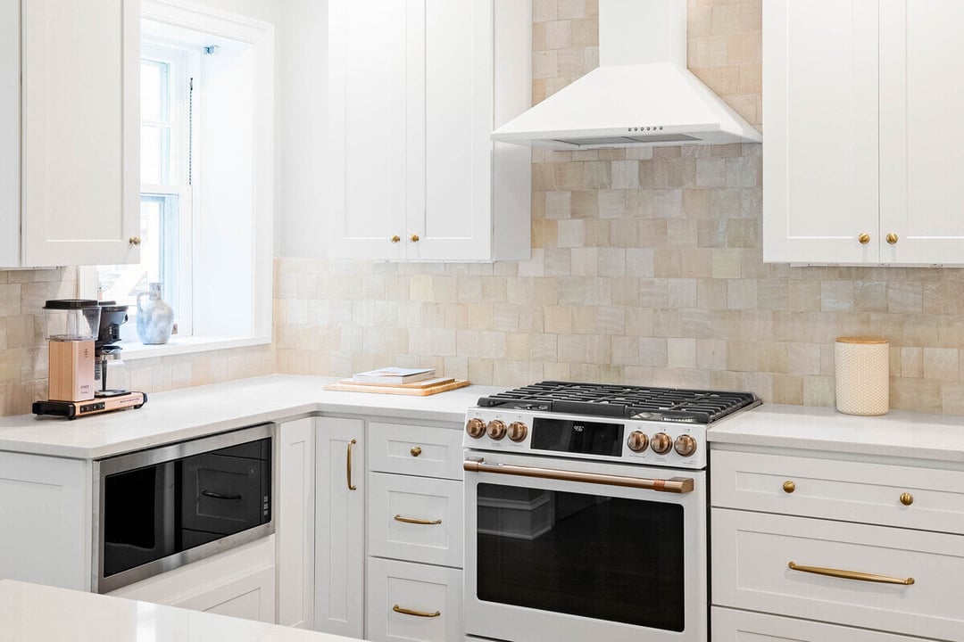 White kitchen with gold hardware, gas range, tile backsplash, and built-in microwave by Bromwell Construction