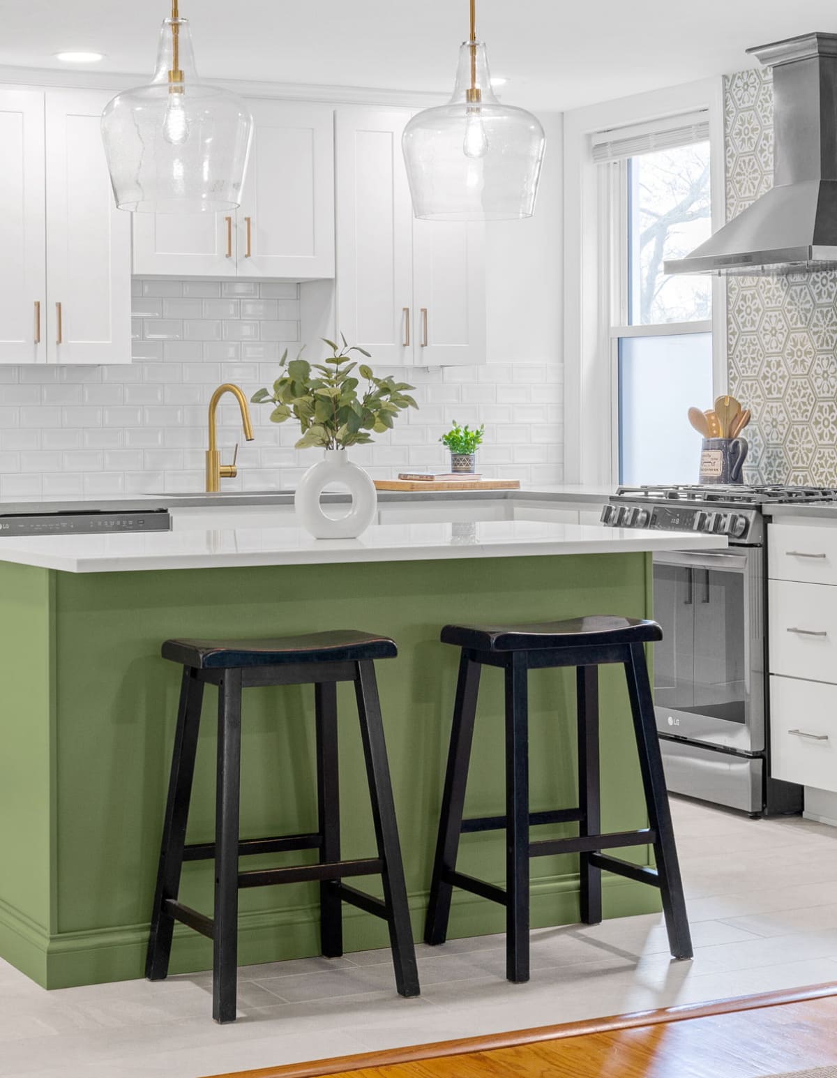 Modern kitchen with green island, white cabinets, brass faucet, glass pendant lights, and black bar stools in a renovated home in Delaware
