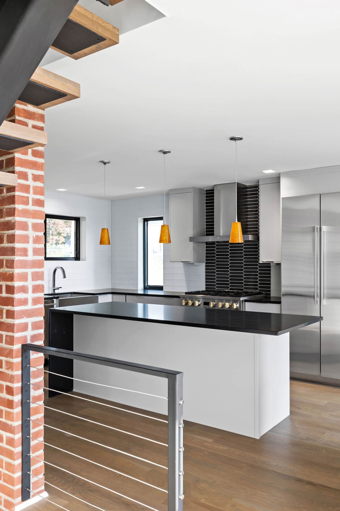 View of black and white kitchen island beneath three orange hanging pendant lights by Bromwell Construction